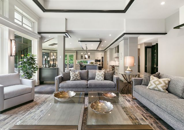 The modern interior of a rental property is pictured in neutral tones, with an open space living room with hardwood floors and grey furniture.